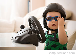 Child wearing a racing helmet and sunglasses, sitting in front of a video game racing wheel.